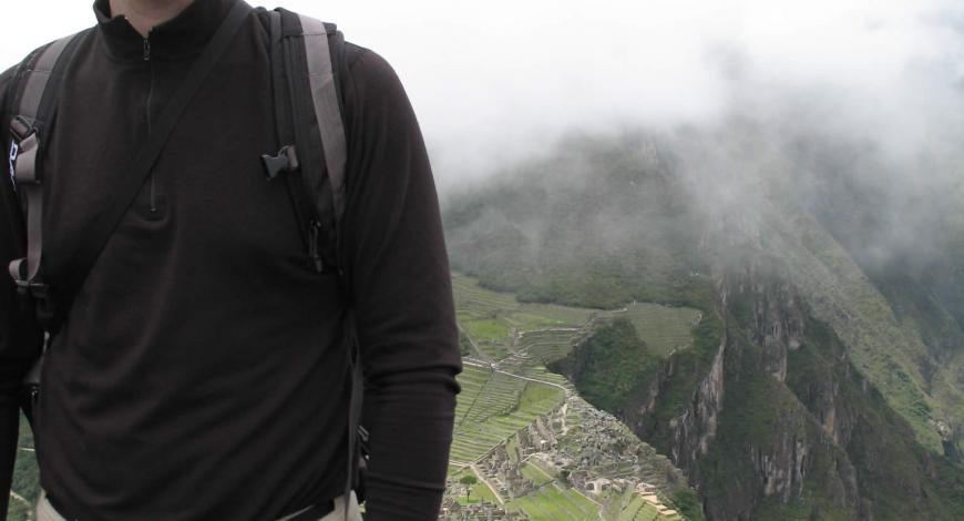 Someone's torso with mountains and clouds in the background